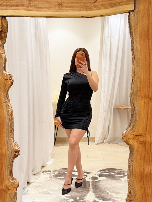 Woman taking a mirror selfie wearing a black dress in a room with wooden frame and white curtains.