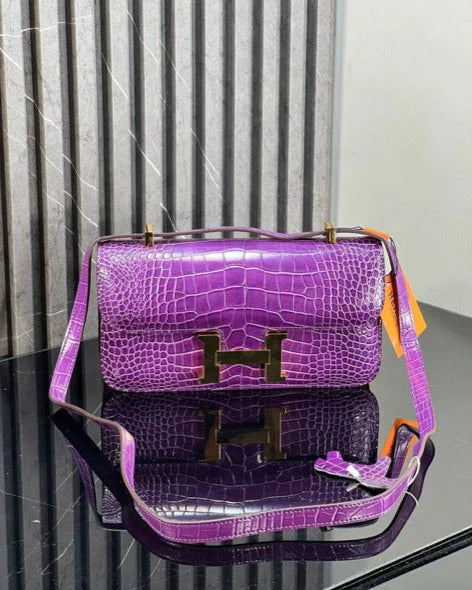 Purple handbag with gold hardware on a reflective surface