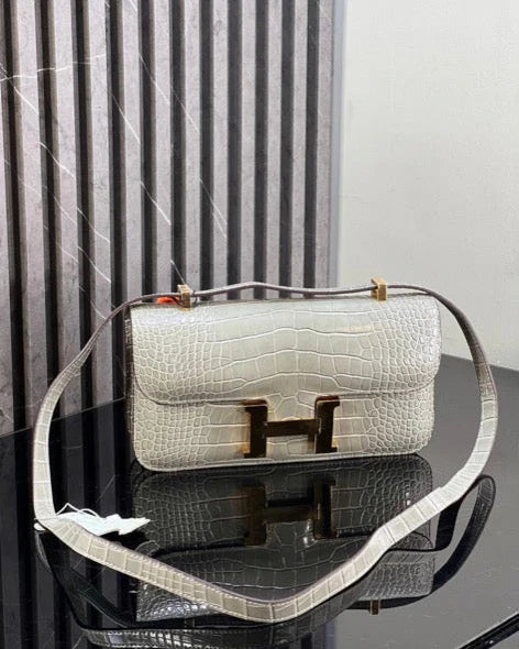 White handbag with gold hardware on a reflective surface, with a neutral background