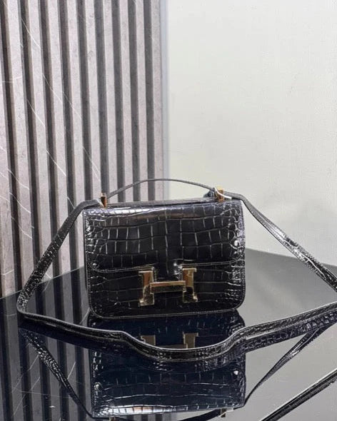 Black crocodile-patterned handbag on a reflective surface with a white background