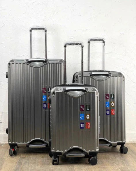 Three silver suitcases of different sizes on a wooden floor with a white wall background.